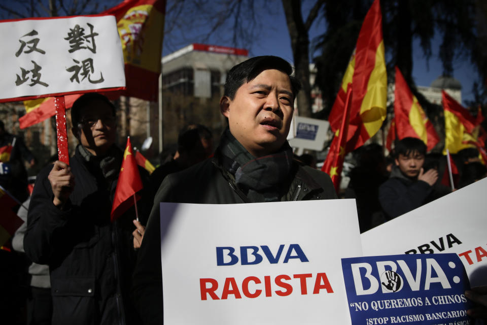 A man protests holding a banner reading in Spanish "BBVA racist" outside a BBVA bank building in Madrid, Spain, Friday, Feb. 15. 2019. Hundreds of Chinese have protested outside a Spanish bank's premises in Madrid, claiming they are being denied access to their accounts while the bank insists it is obeying money-laundering laws. (AP Photo/Andrea Comas)