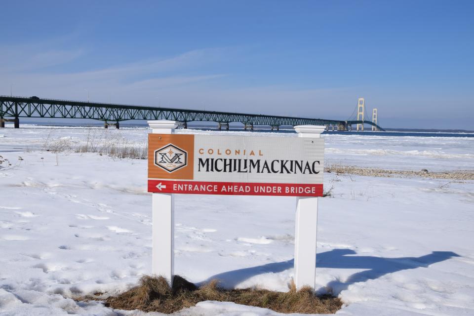 A Colonial Michilimackinac sign is photographed in front of the Mackinac Bridge. People can visit the historic fort in Mackinaw City.