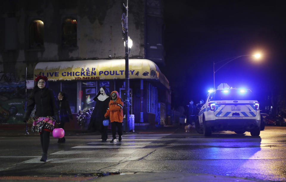 Trick-or-treaters walk past a crime scene in the 3700 block of West 26th Street, where a 7-year-old girl was shot while trick-or-treating Thursday, Oct. 31, 2019, in Chicago. A 7-year-old girl out trick-or-treating in a bumblebee outfit was critically injured Thursday night during a shooting on Chicago's West Side. (John J. Kim/Chicago Tribune via AP)