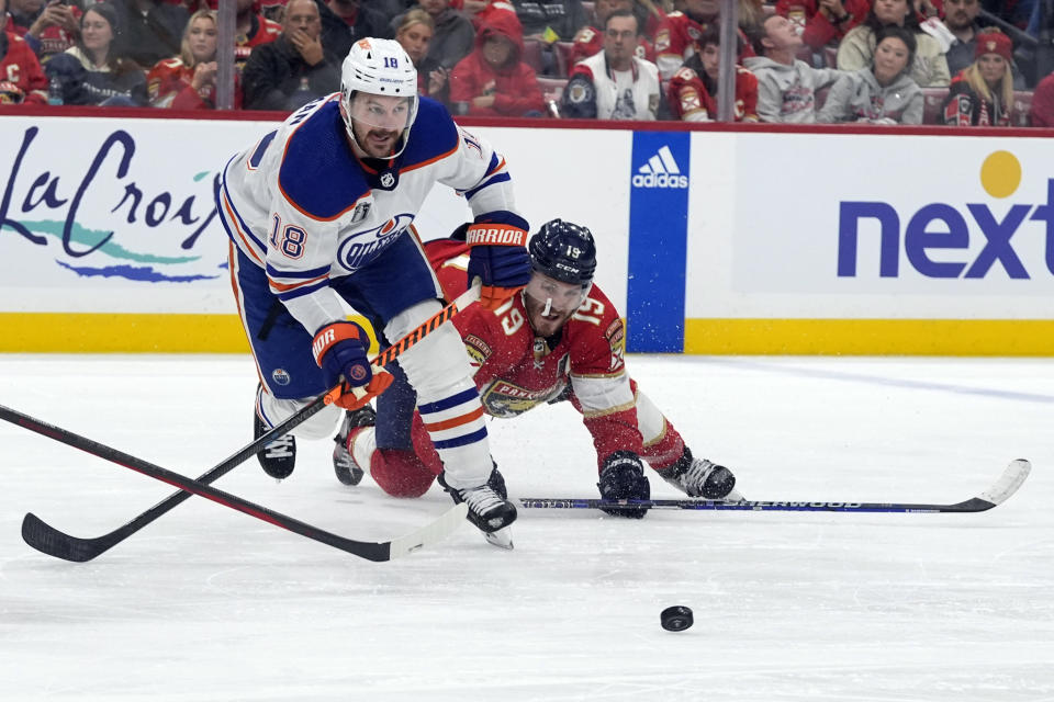 Edmonton Oilers left wing Zach Hyman (18) goes for the puck as Florida Panthers left wing Matthew Tkachuk (19) falls to the ice during the third period of Game 1 of the NHL hockey Stanley Cup Finals Saturday, June 8, 2024, in Sunrise, Fla. (AP Photo/Wilfredo Lee)