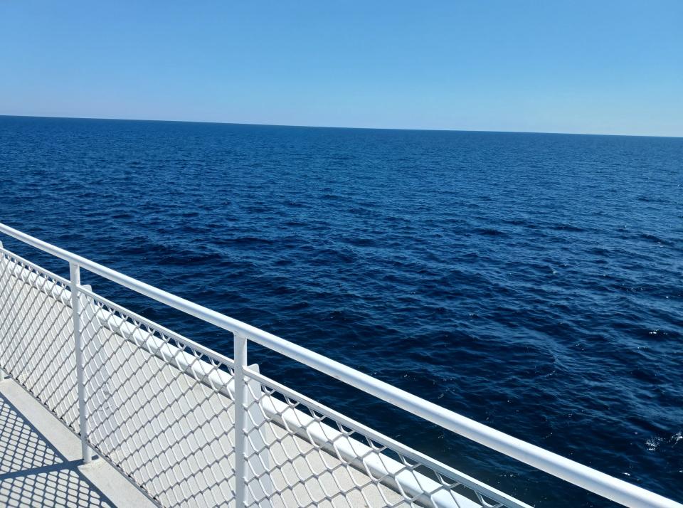 View of blue waters from over a ferry balcony with a fence