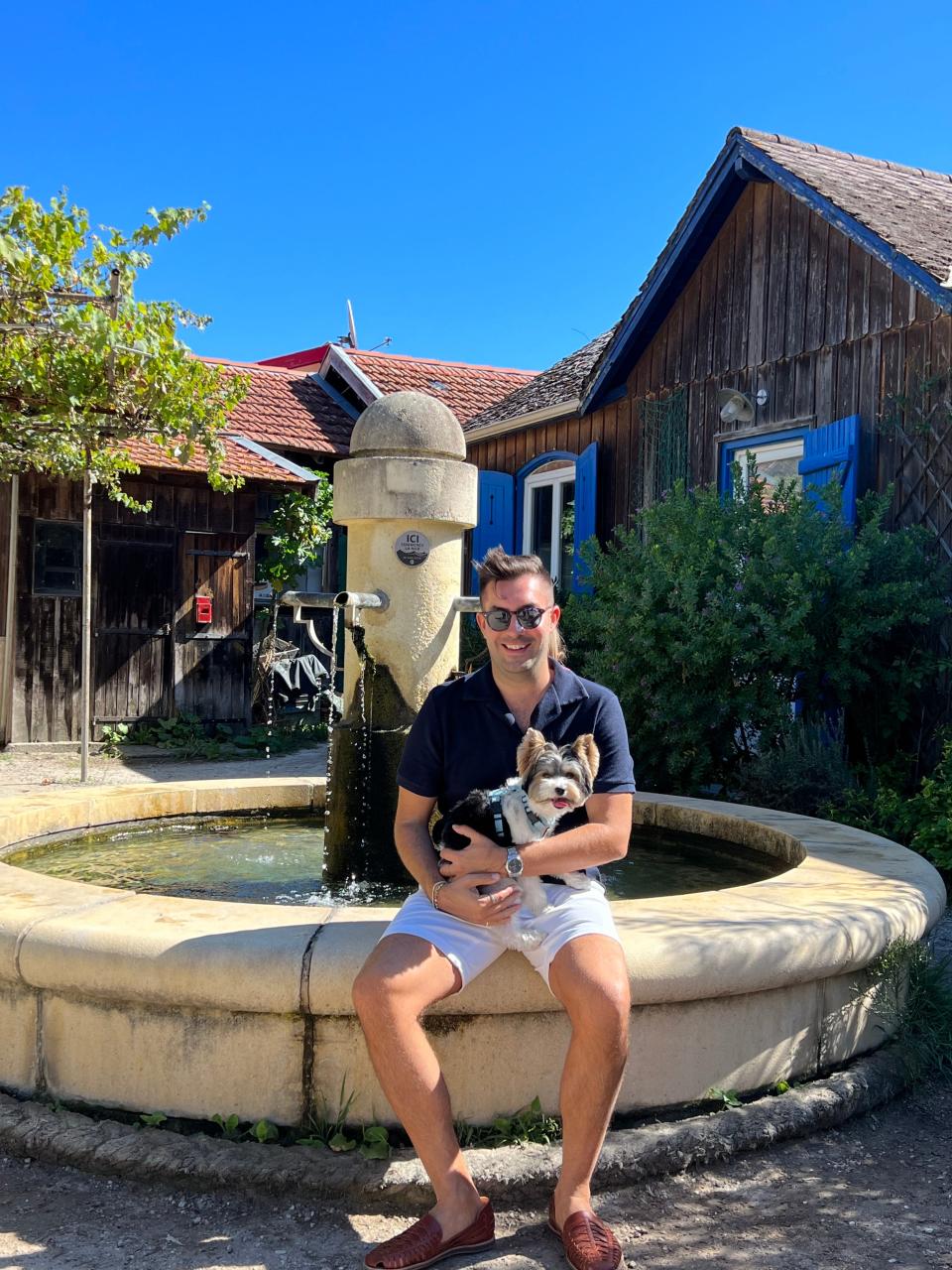 Man sitting on the edge of a fountain holding a dog and smiling in Cap-Ferret, France