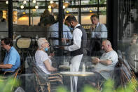 A waiter wearing a face mask to protect against coronavirus serves at a restaurant terrace in Paris, Monday, July 26, 2021. France's parliament approved a law requiring special virus passes for all restaurants and domestic travel, and mandating vaccinations for all health workers. (AP Photo/Michel Euler)