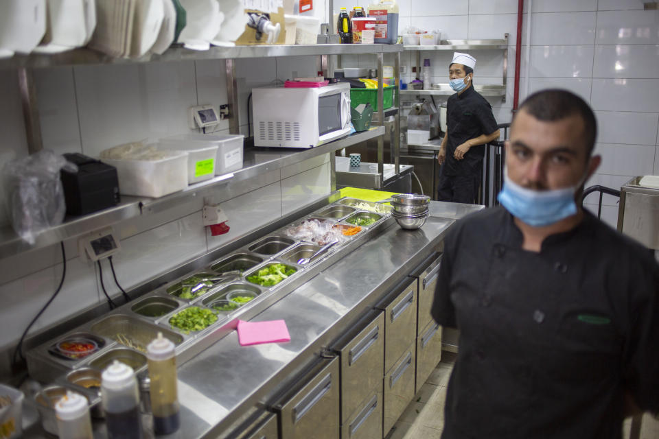 Employees work in the kitchen of Go Noodles wear face masks due the coronavirus outbreak in Tel Aviv Israel, Thursday, July 16, 2020. The coronavirus crisis and its economic impact have forced many small businesses and restaurants to shut their doors in recent months, but Tel Aviv's Go Noodles opened a new branch last week that features digital-only ordering and pickup from lockers. (AP Photo/Ariel Schalit)