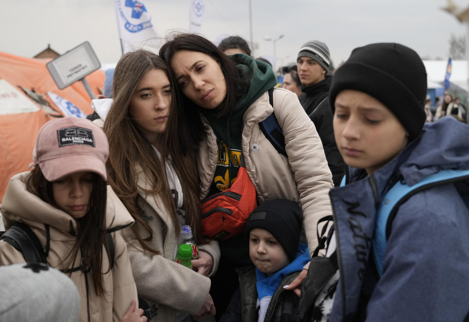 Ukrainian refugees, looking anxious, wait in line at a border crossing.