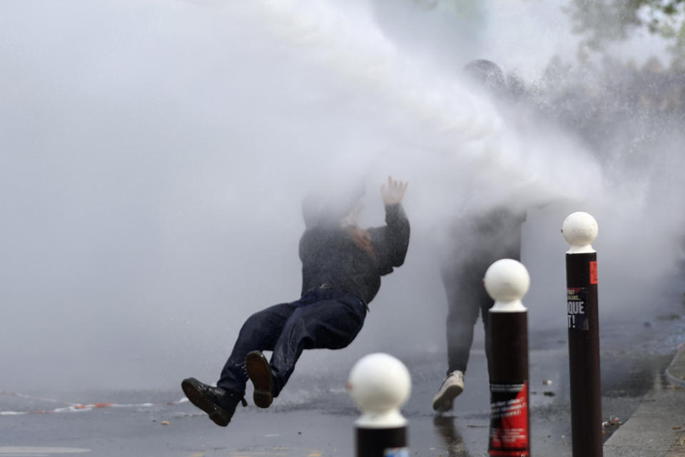 A protester is overthrown as police forces use water canon during a demonstration, Monday, May 1, 2023 in Paris. Across France, thousands marched in what unions hope are the country's biggest May Day demonstrations in years, mobilized against President Emmanuel Macron's recent move to raise the retirement age from 62 to 64. (AP Photo/Aurelien Morissard)