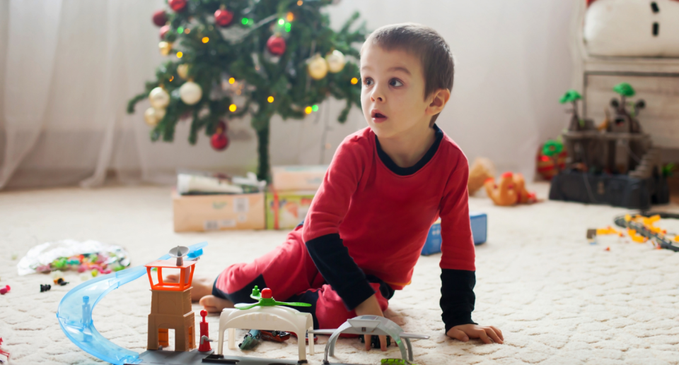 little boy in red pjs playing with toys sitting on floor in front of christmas tree 