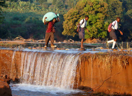 School children and a man carrying food aid cross a river after Cyclone Idai at Coppa business centre in Chipinge, Zimbabwe, March 26,2019. REUTERS/Philimon Bulawayo