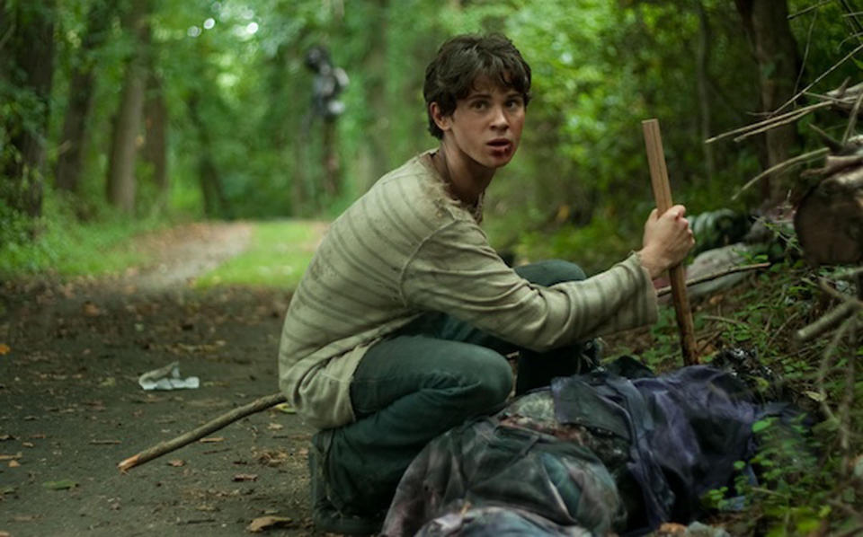 A young man removes a stake from the chest of a vampire’s corpse near a dirt road