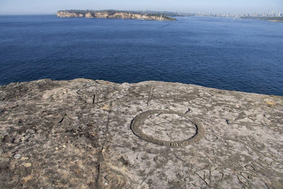 Inscriptions carved near the edge of a cliff with Sydney's skyline in the distance.