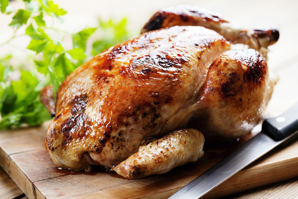 Crockpot whole chicken on a cutting board with a cutting knife with fresh herbs in the background