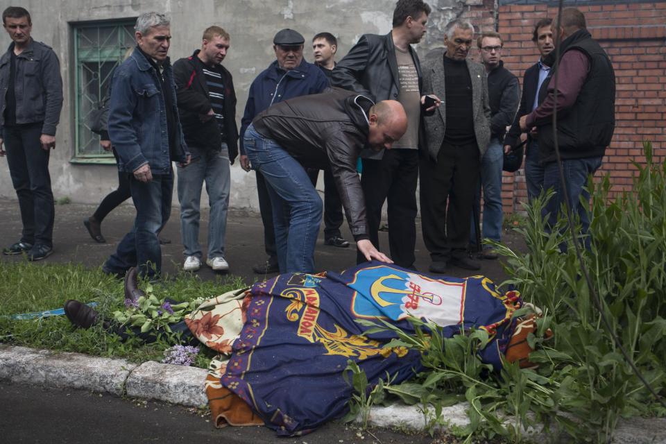 The body of a police officer killed during fighting between government forces and insurgents is covered with the flag of Mariupol as it lies outside a police station in Mariupol, eastern Ukraine, Friday, May 9, 2014. Fighting exploded Friday in Mariupol, a city of 500,000 on the Sea of Azov that is on the main road between Russia proper and Crimea. The fighting between government forces and insurgents in Mariupol has left several people dead. (AP Photo/Alexander Zemlianichenko)