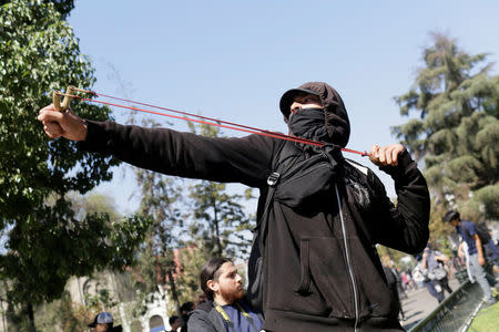 A demonstrator with a slingshot clashes with riot police during a protest demanding an end to profiteering in the education system in Santiago, Chile April 19, 2018. REUTERS/Pablo Sanhueza