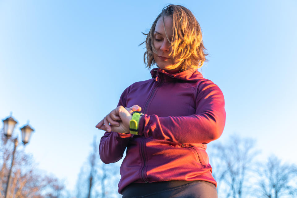 Female sportswoman in red sports wear monitoring and looking at wrist smartwatch screen. Low angle view