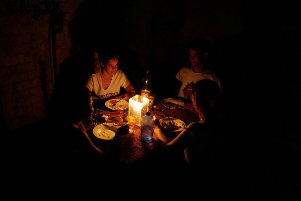 Tres personas de una familia sentdas a la mesa, todo está a oscuras y se alumbran con velas.