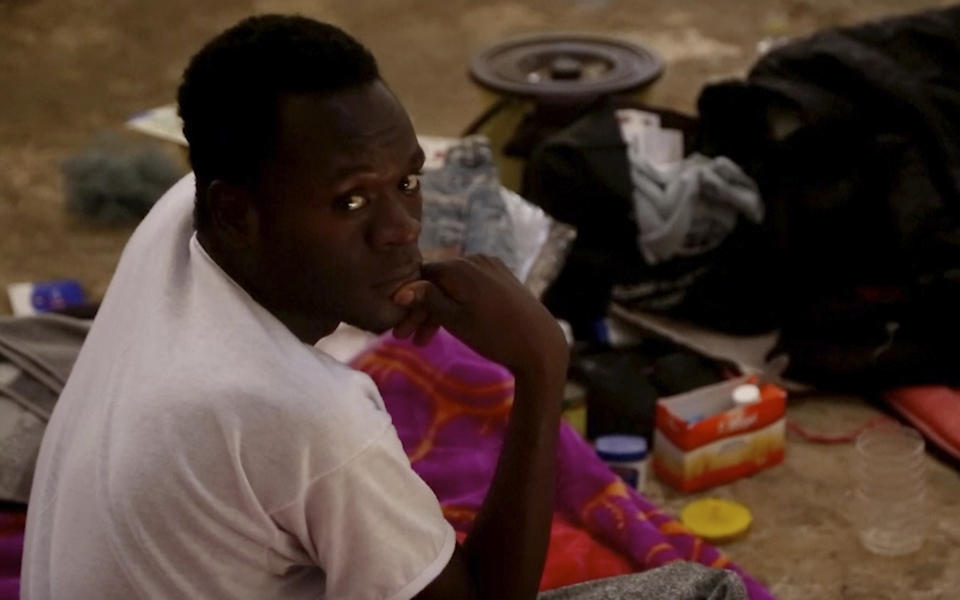 In this Wednesday, July 17, 2019 frame grab from video, a migrant sits on the floor in a detention center in the city of Sabha, which is about 650 kilometers, or 400 miles, south of the capital, Tripoli, Libya. Migrants held at a small, dilapidated detention center in the southern Libyan city of Sabha say they are being neglected by international organizations and often go hungry due to lack of food. (AP Photo)