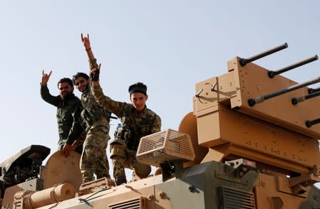 Members of Syrian National Army, known as Free Syrian Army, react as they drive on top of an armored vehicle in the Turkish border town of Ceylanpinar