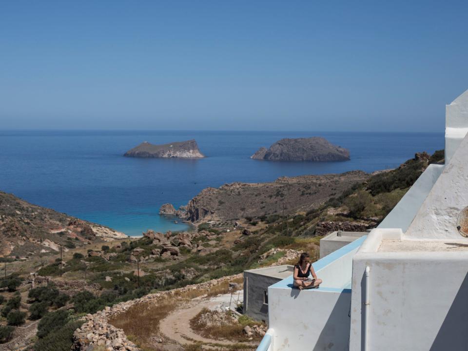 A person reading a book on a terrace overlooking blue waters in Greece