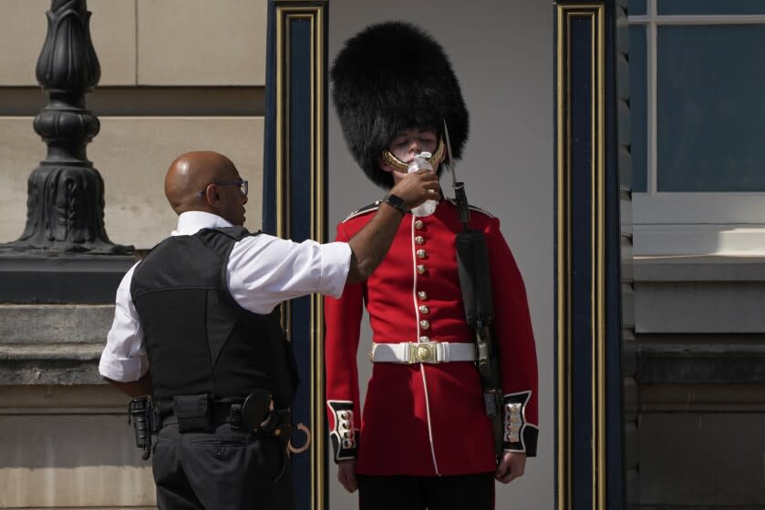 A police officer givers water to a British soldier wearing a traditional bearskin hat, on guard duty outside Buckingham Palace, during hot weather in London, Monday, July 18, 2022. The British government have issued their first-ever "red" warning for extreme heat. The alert covers large parts of England on Monday and Tuesday, when temperatures may reach 40 degrees Celsius (104 Fahrenheit) for the first time, posing a risk of serious illness and even death among healthy people, the U.K. Met Office, the country's weather service, said Friday. (AP Photo/Matt Dunham)