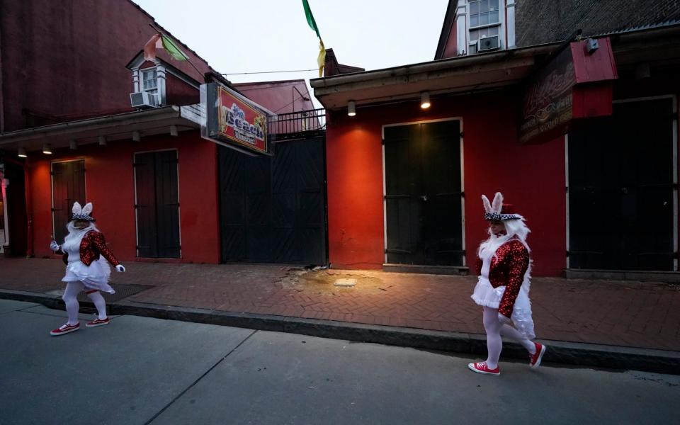 People in costume walk past a shuttered bar on Bourbon Street in the French Quarter of New Orleans - AP