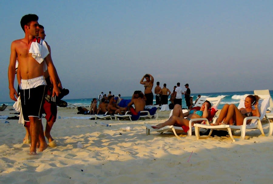 US students walk on the beach as they watch girls sunbathing during spring break at Cancun beach, Mexico, Monday March 17, 2003. Thousands of US students came to Cancun to enjoy spring break unconcerned about terrorism and a possible war in Iraq. Authorities however, are concerned that Cancun, a narrow peninsula packed with young Americans, could be the perfect terrorist target, and they have beefed up security to prepare for anything. (AP Photo/Jose Luis Magana)