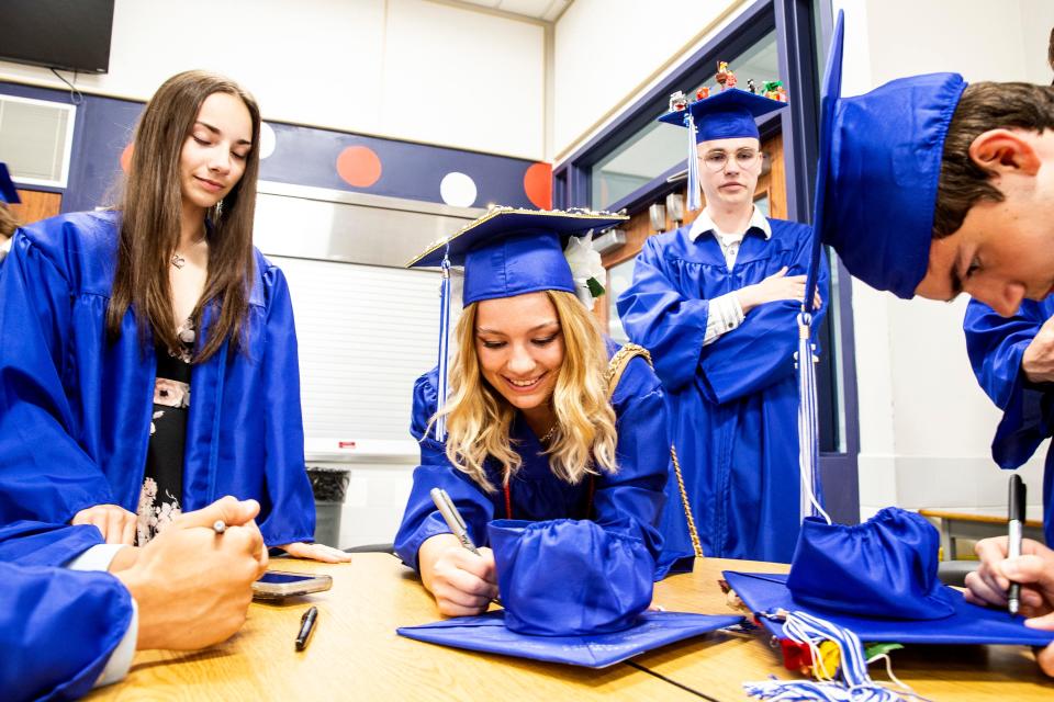 From left, graduates Bree Young, Andie Przybycien, John Underhill, and Deacon Jacobson sign their names on there graduation caps, on June 7, 2022, prior to the start of the 2022 Fort LeBoeuf High School commencement at Carm Bonito Field in Waterford, PA.