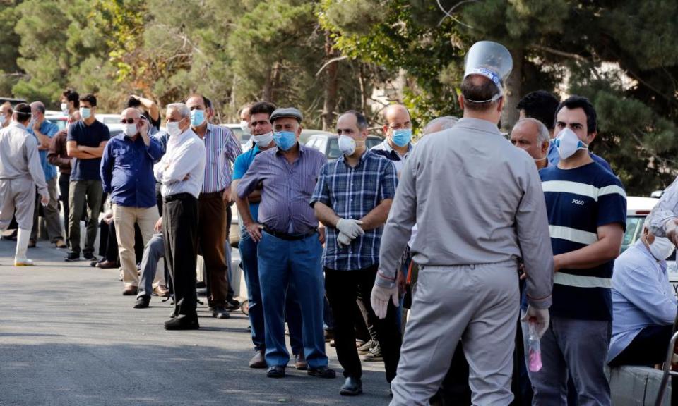 ranians wearing face masks wait in a line outside a cattle market in Hakimieh