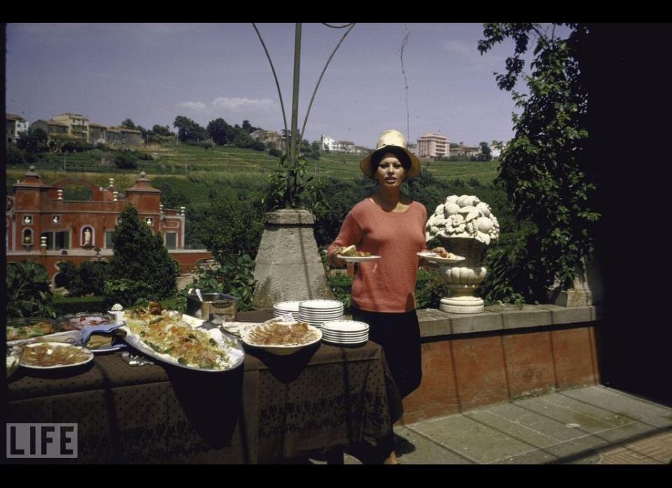 Loren prepares for an al fresco lunch on the terrace. The background shows the villa's exterior and the nearby village of Marino.