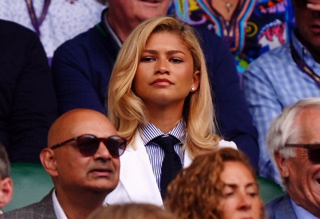 Woman with blonde hair wearing a blue and white striped shirt and dark tie with white jacket