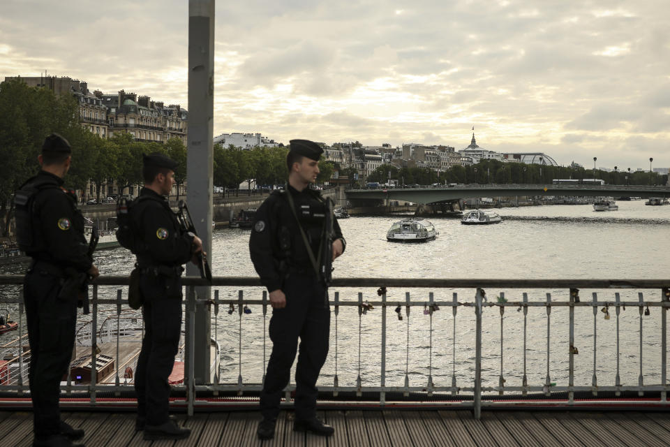 Police officers stand on a bridge as barges cruise on the Seine river during a rehearsal for the Paris 2024 Olympic Games opening ceremony, Monday, June. 17, 2024 in Paris.The river will host the Paris 2024 Olympic Games opening ceremony on July 26 with boats for each national delegation. (AP Photo/Thomas Padilla)