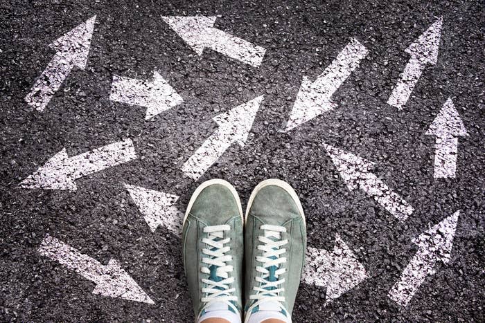 Sneaker shoes and arrows pointing in different directions on asphalt ground, choice concept