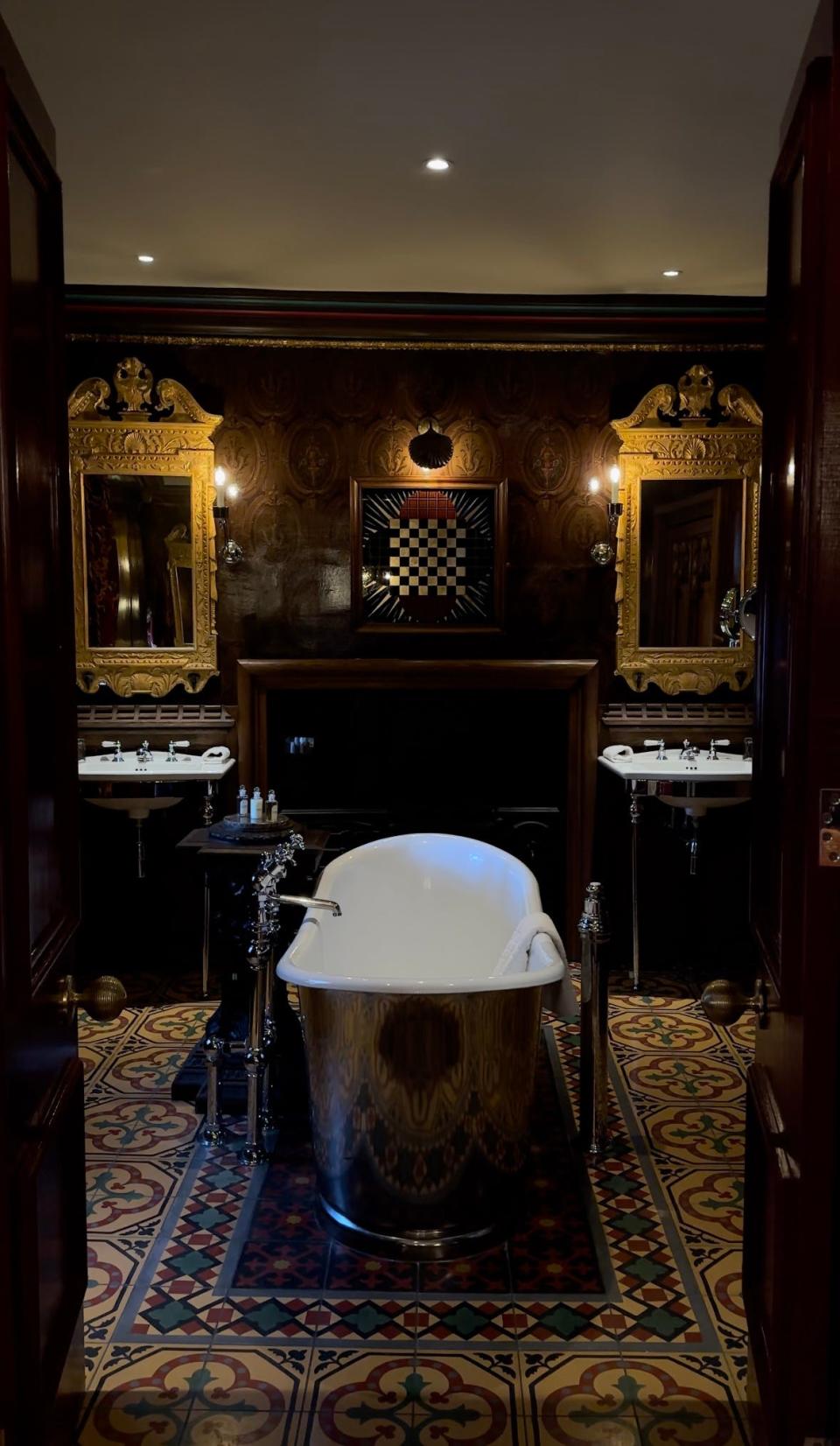 A bathroom with free-standing silver bathtub and twin sinks.