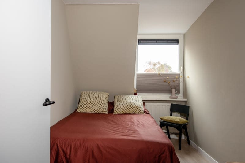 Angled ceiling, red bedding with cream pillow cases, small wood chair in corner