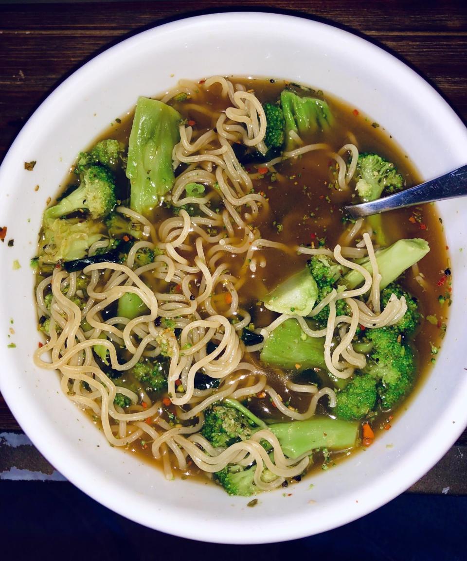 A bowl of noodle soup with broccoli florets and a spoon