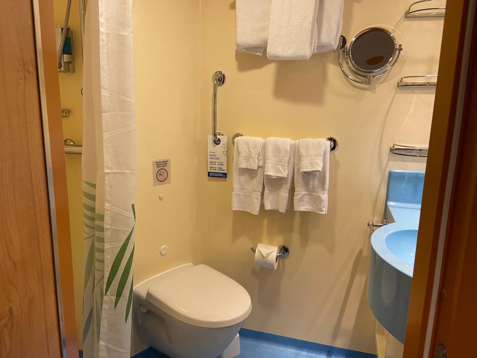 A cruise ship bathroom with a toilet, sink, and towels, and a shower curtain.