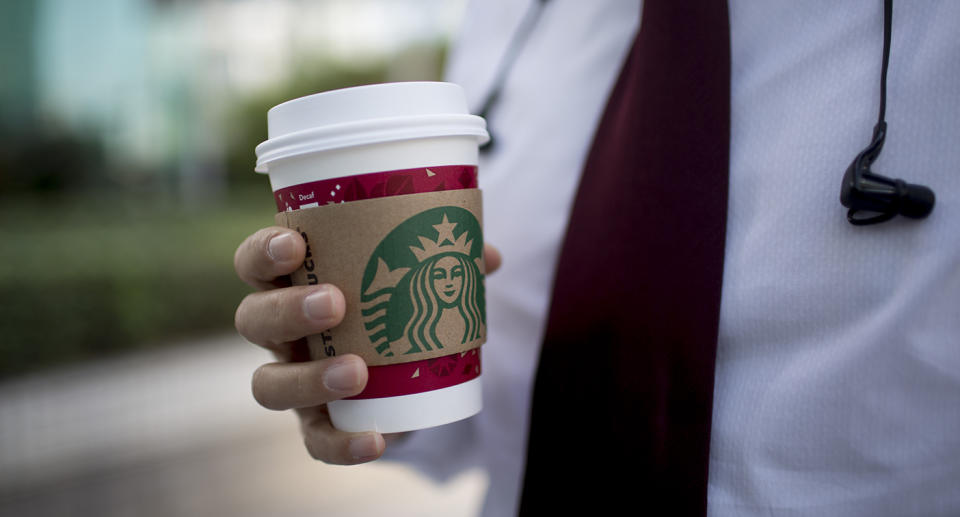 A man holds a disposable Starbucks coffee cup