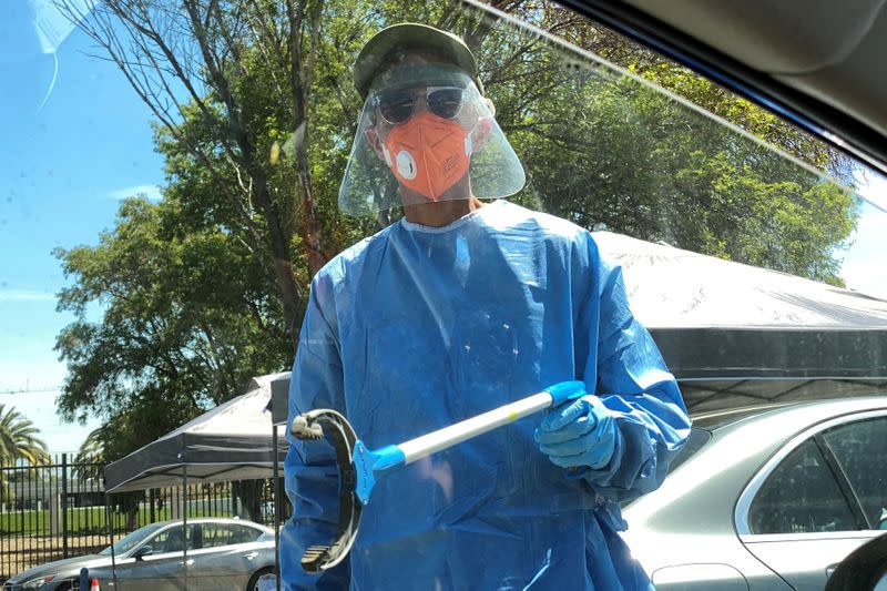 FILE PHOTO: A healthcare worker reaches toward a car to grab a completed coronavirus diagnostic test, as the global outbreak of the coronavirus disease (COVID-19) continues, in Los Angeles