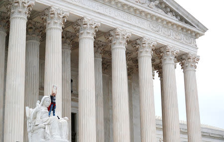 A protester stands on the lap of "Lady Justice" on the steps of the U.S. Supreme Court building holding up a "Believe Survivors" sign as demonstrators storm the steps and doors of the Supreme Court while Judge Brett Kavanaugh is being sworn in as an Associate Justice of the court inside on Capitol Hill in Washington, U.S., October 6, 2018. REUTERS/Carlos Barria