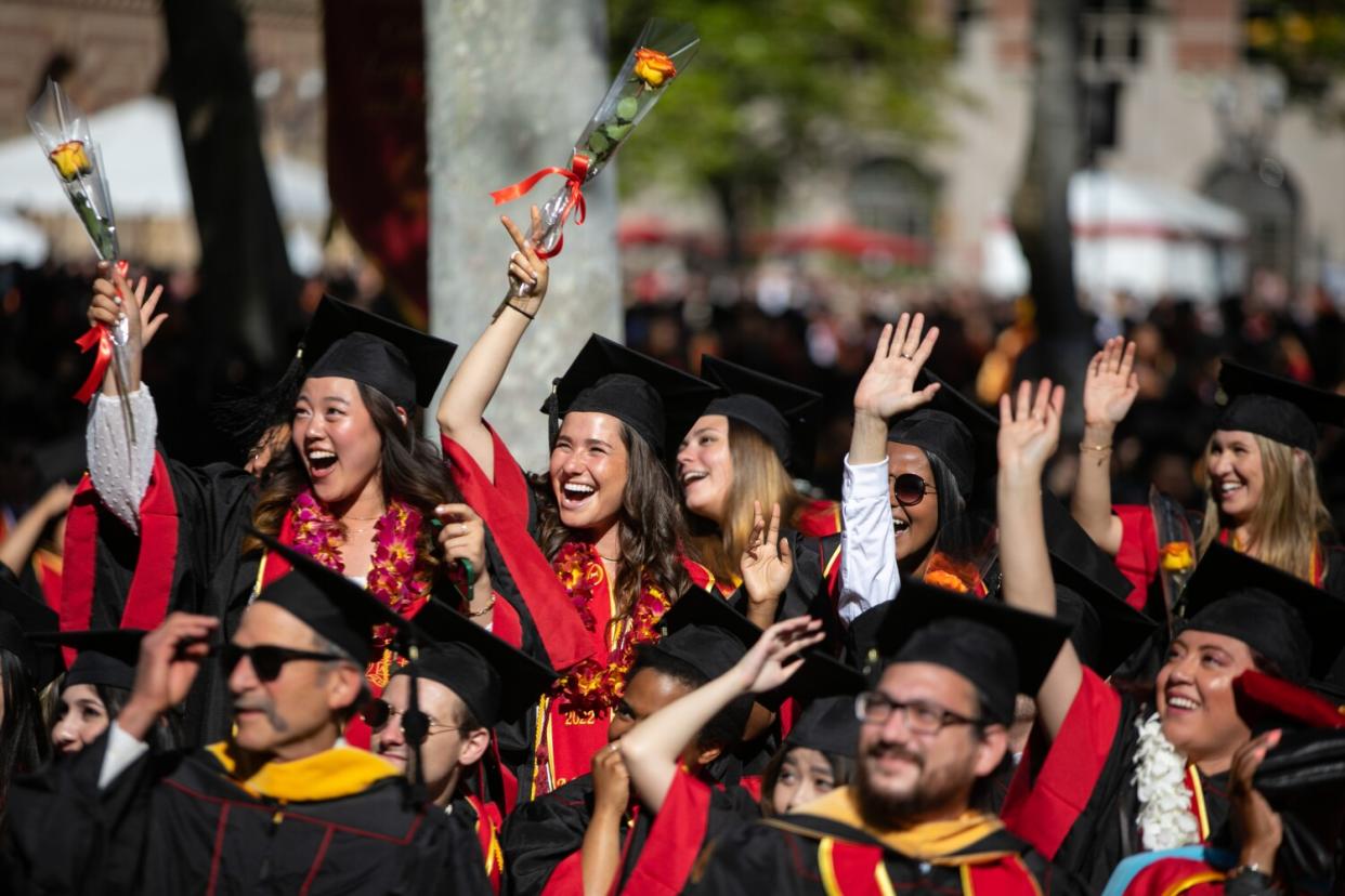 A crowd in caps and gowns cheers, some holding roses.