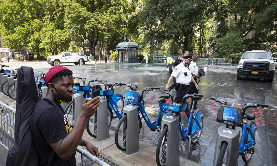 Jonathan Lykes, left, watches as police walk across a park adjacent to City Hall, Wednesday, July 22, 2020, in New York. Police in riot gear cleared the month-long encampment of protesters and homeless people from the park earlier Monday morning. Lykes says he was one of the organizers of the encampment. (AP Photo/Mark Lennihan)