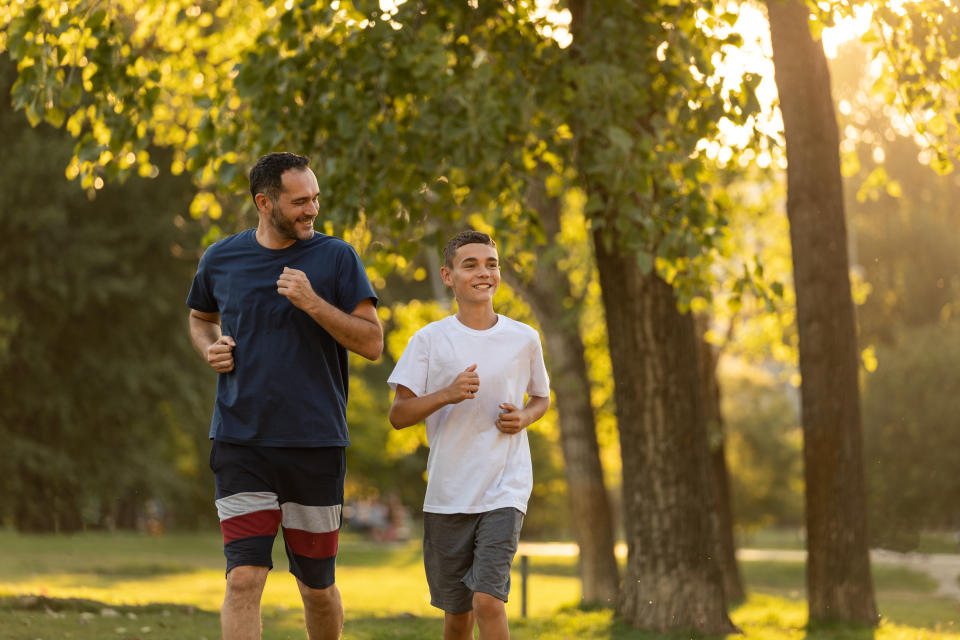 Father and teen son embrace a healthy lifestyle, front view of their jogging activity in the park.