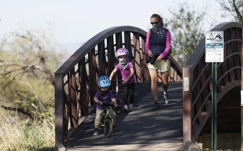 A woman and children wear face coverings as a precaution against the coronavirus while crossing a bridge in Barr Lake State Park Sunday, May 17, 2020, near Brighton, Colo. (AP Photo/David Zalubowski)