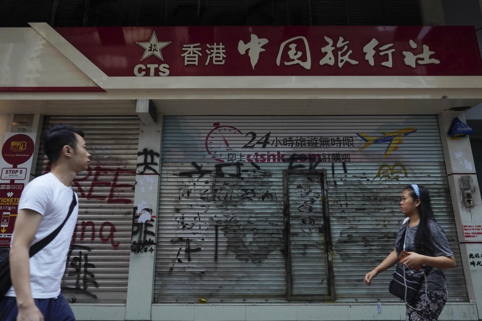 FILE - In this Oct. 7, 2019, file photo, pedestrians look at graffiti in front of China Travel Service in Hong Kong. Hong Kong’s embattled leader Carrie Lam said Tuesday that the city’s economy is being battered by months of increasingly violent protests. (AP Photo/Vincent Yu, File)