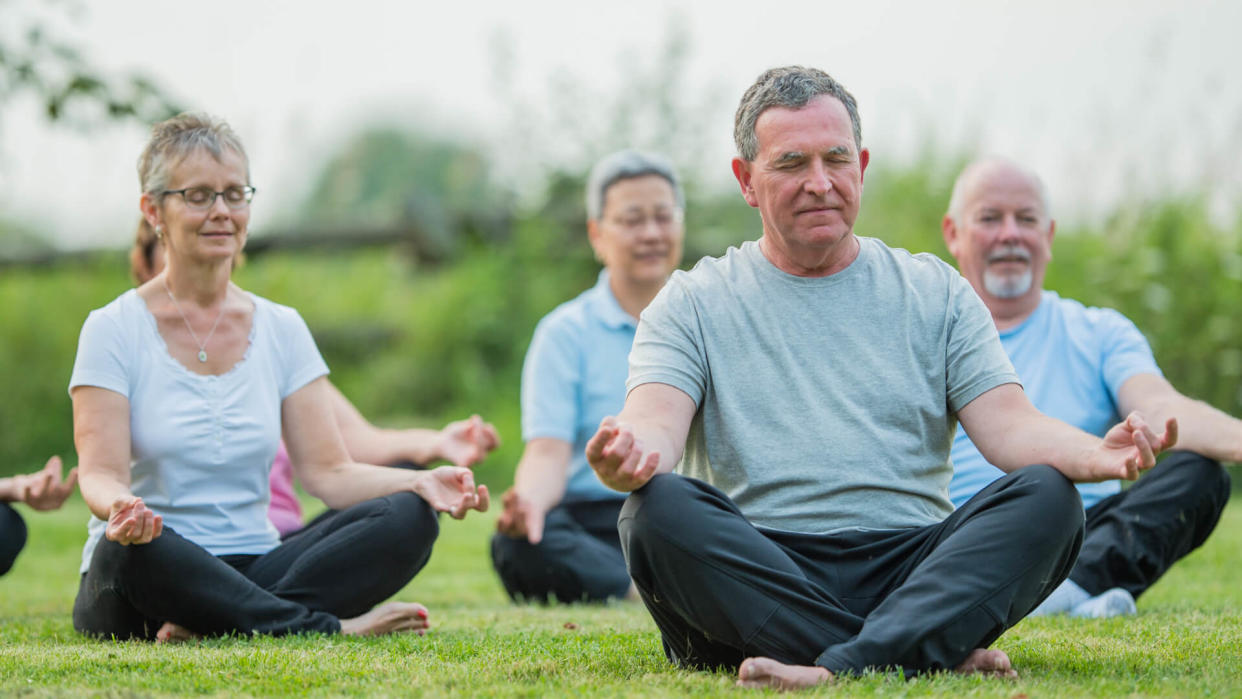 A multi-ethnic group of senior adults are taking a tai chi fitness class.