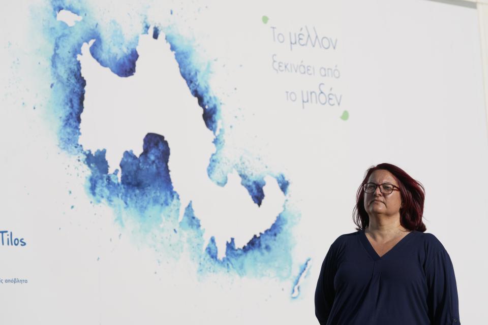 Tilos Mayor Maria Kamma-Aliferi poses for a photograph in front of the island's map as the phrase reads in Greek "The future starts from zero" at a recycling plant built on old landfill site on the Aegean Sea island of Tilos, southeastern Greece, Monday, May 9, 2022. When deciding where to test green tech, Greek policymakers picked the remotest point on the map, tiny Tilos. Providing electricity and basic services, and even access by ferry is all a challenge for this island of just 500 year-round inhabitants. It's latest mission: Dealing with plastic. (AP Photo/Thanassis Stavrakis)