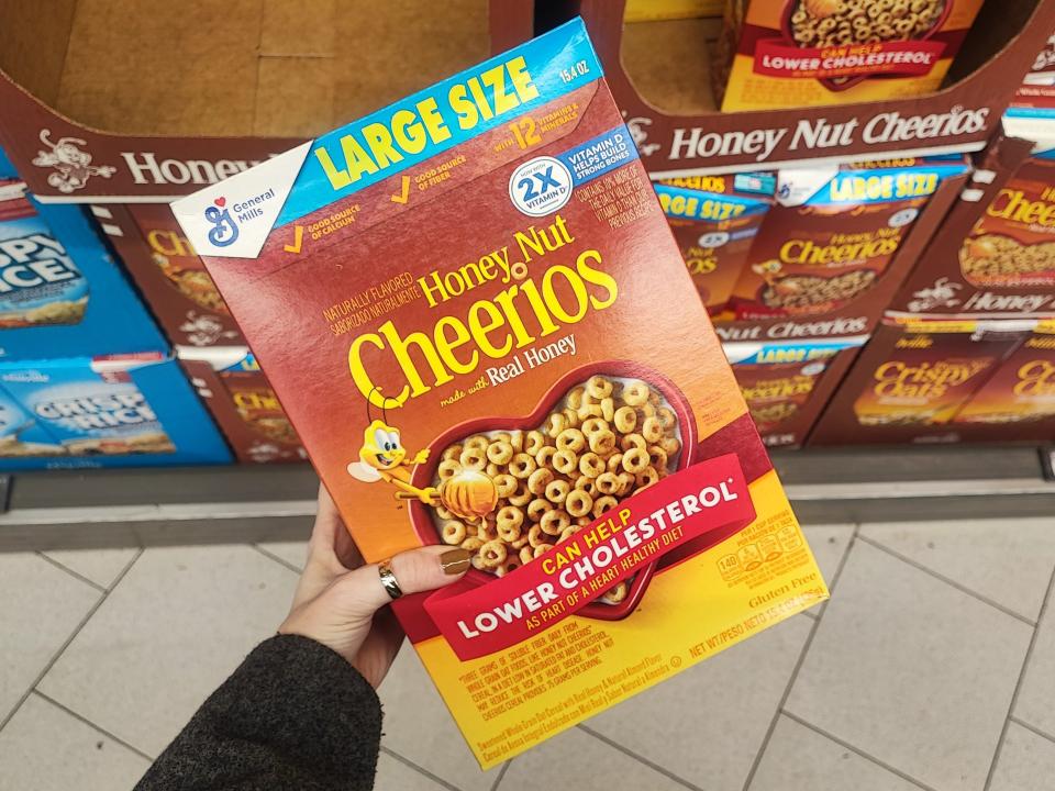 A hand holding a large box of Honey Nut Cheerios