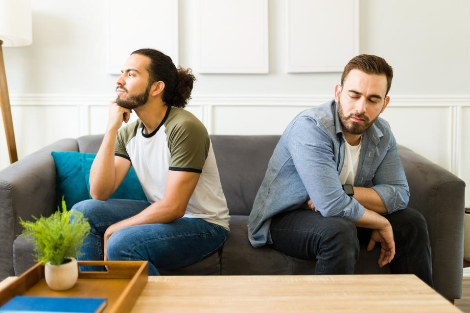 Angry gay man looking upset with his boyfriend and having communication problems while arguing in the living room