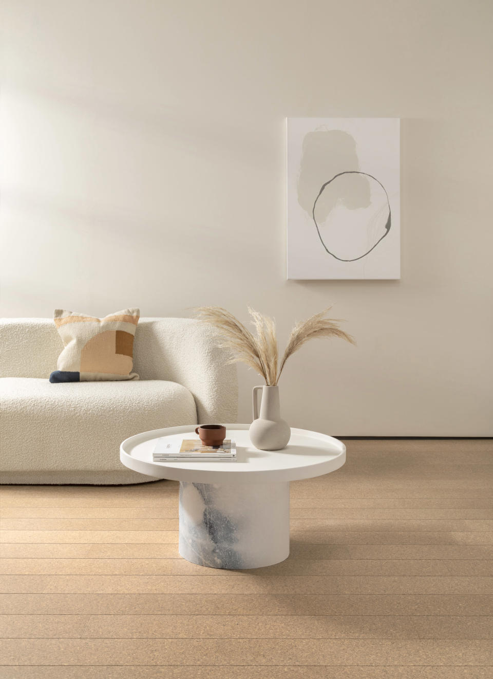 A neutral themed living room with a boucle sofa, white coffee table and cork flooring