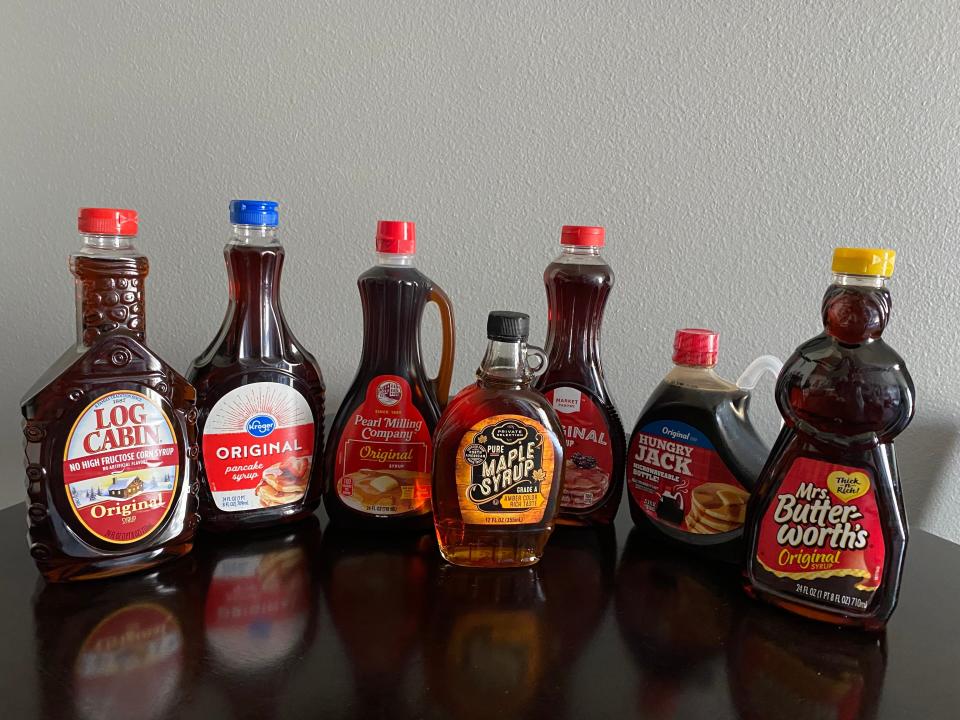 six bottles of pancake syrup and one bottle of real maple syrup lined up on a counter