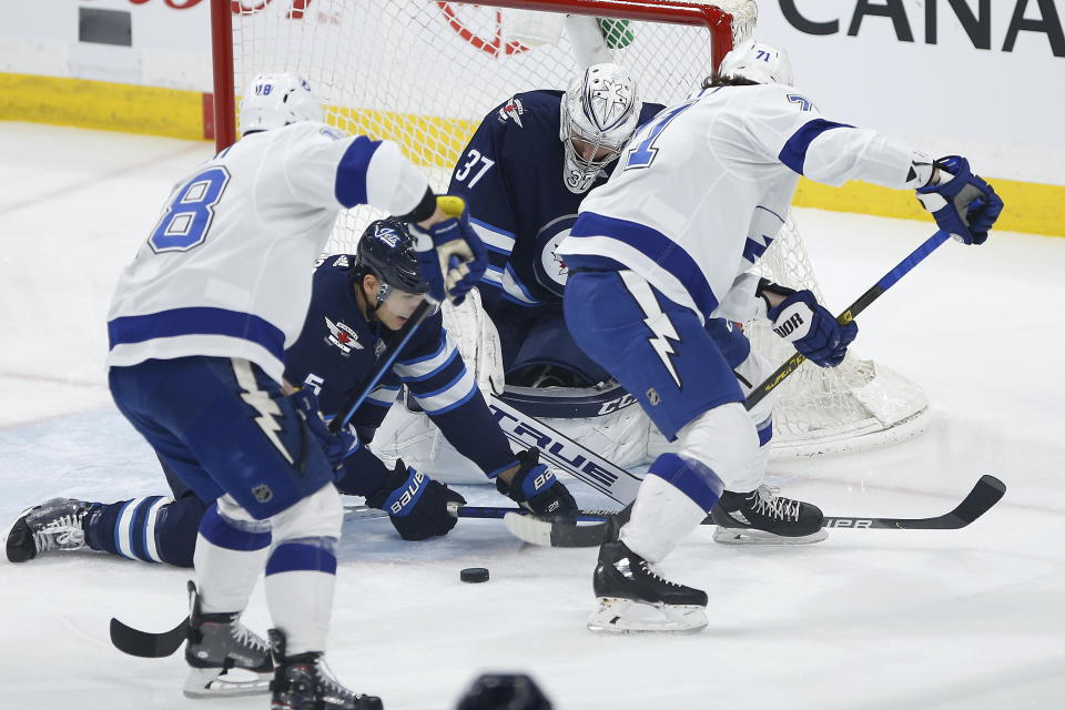 Winnipeg Jets goaltender Connor Hellebuyck (37) watches the puck Tampa Bay Lightning's Ondrej Palat (18) and Anthony Cirelli (71) look for the rebound and Jets' Luca Sbisa (5) defends during first-period NHL hockey game action in Winnipeg, Manitoba, Friday, Jan. 17, 2020. (John Woods/The Canadian Press via AP)